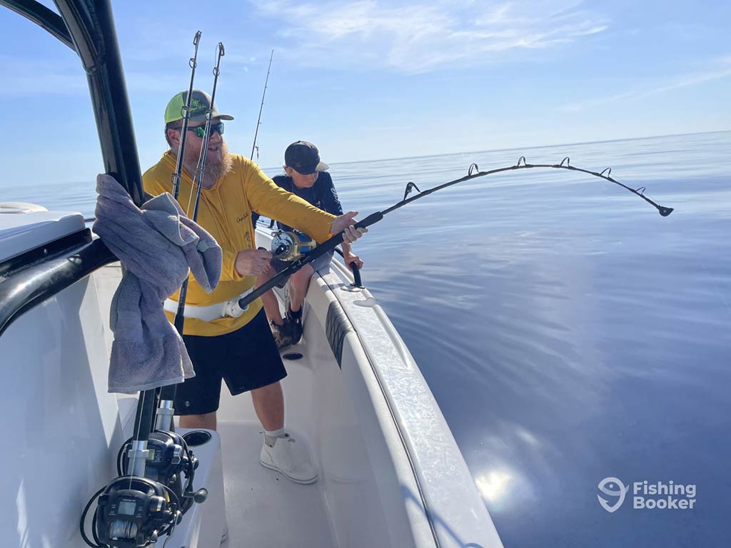 An angler in yellow attempts to do battle off the side of a fishing boat in calm offshore waters, using a large, heavy-duty offshore fishing rod on a sunny day on a trip from Crystal River