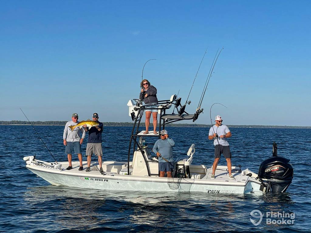 A view across the water to a center console fishing boat in the inshore waters near Santa Rosa Beach with a group of anglers posing and fishing, and one holding a Redfish on a clear day