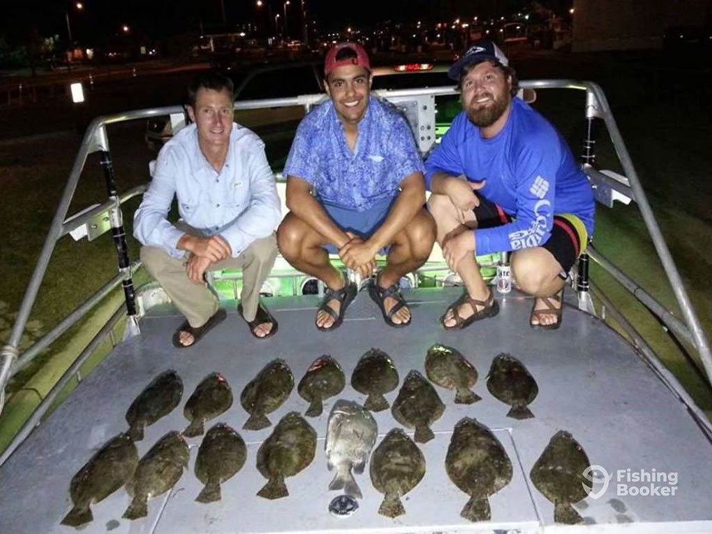 Three anglers crouch on an aluminum fishing charter behind a large selection of Flounder, caught while night fishing out of Aransas Pass