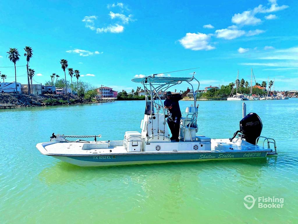 A view across the turquoise waters of Port Isabel to a center console boat that operates as an inshore fishing charter, with the captain busy at the wheel on a clear day