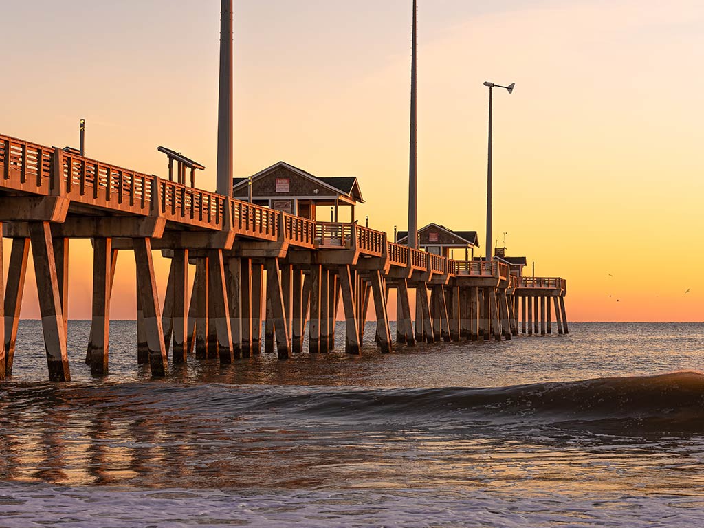 A view from the beach towards the ocean, with Jannette's Pier visible on the left of the image, stretching out into the Atlantic from Nag's Head at sunset on a clear day