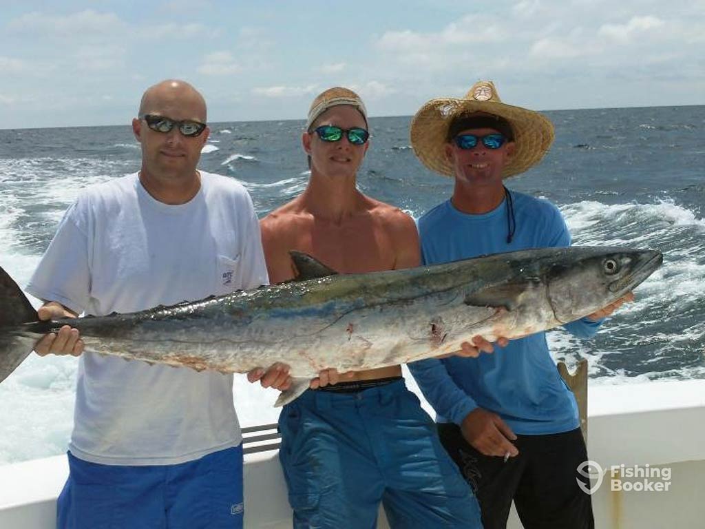 Three anglers leaning on the side of a fishing charter out of Santa Rosa Beach holding a large King Mackerel with the water behind them on a clear day