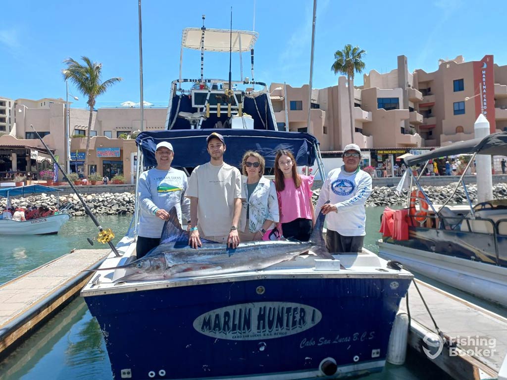 A group of anglers posing on the deck of a sportfishing boat whiole back on deck in Cabo San Lucas behind a Marlin on a sunny day