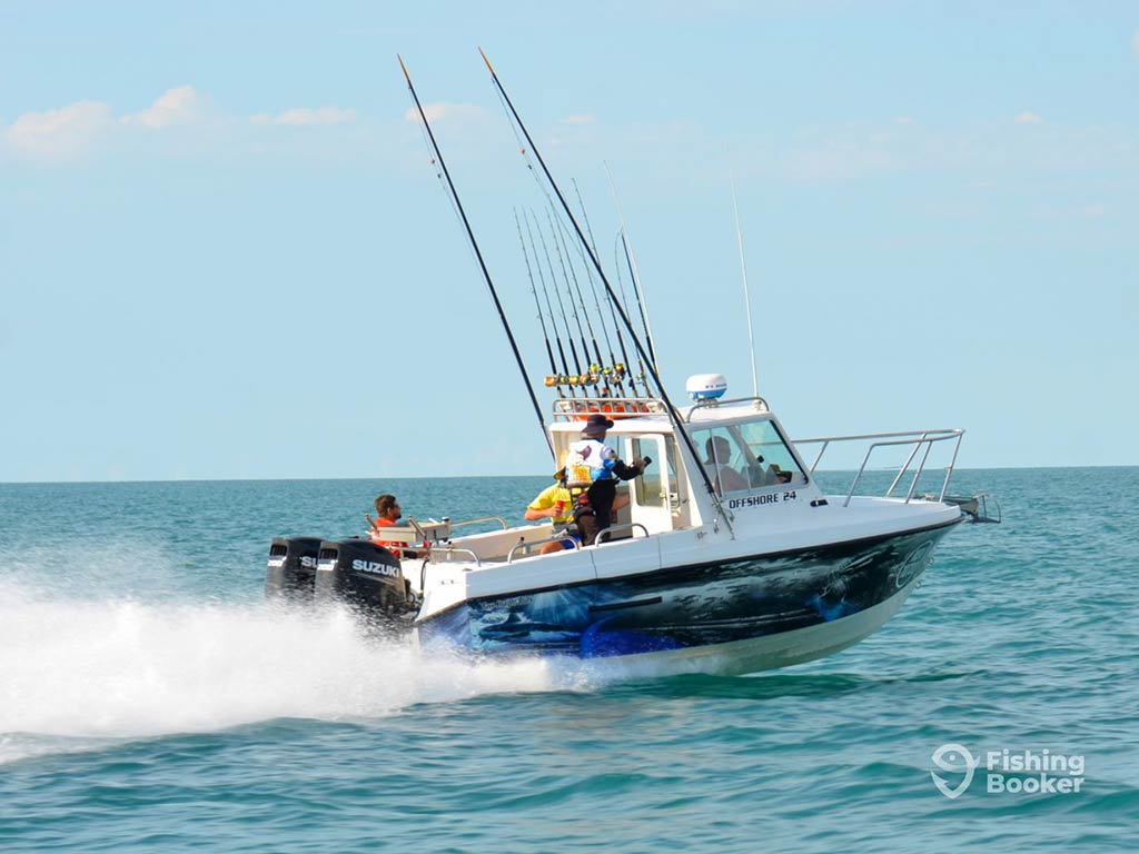 A charter fishing boat, complete with trolling rods, sailing to the deep seas off the northern coast of Australia on a sunny day, leaving behind a big wake