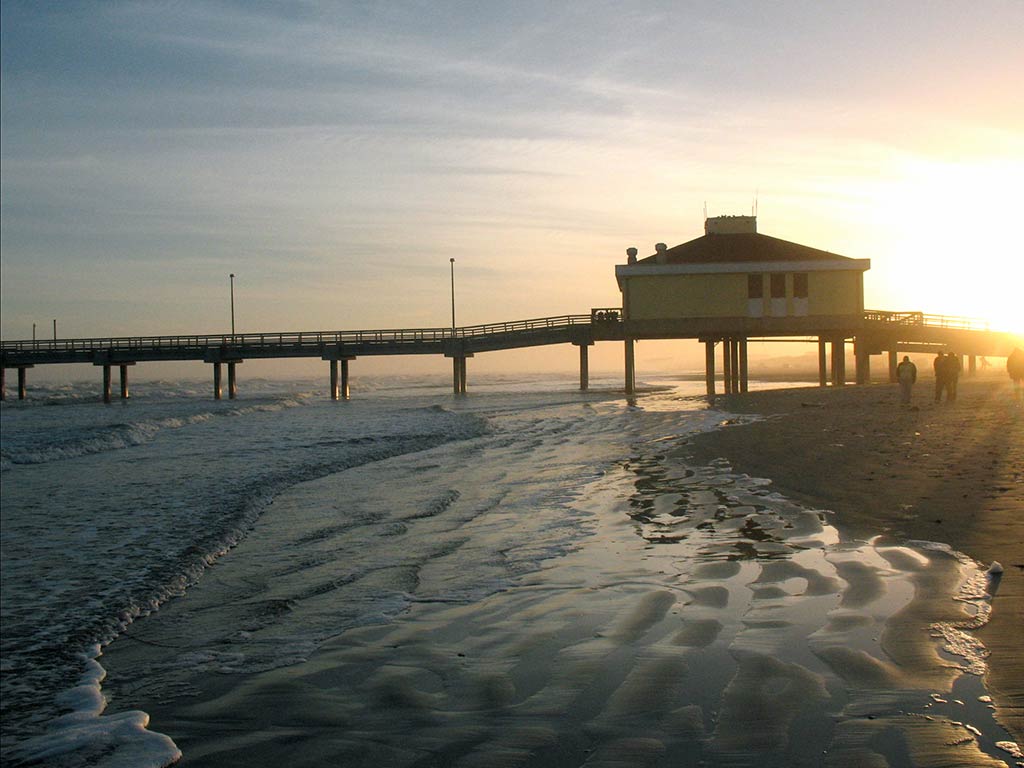 A view across the beach towards a fishing pier in the Gulf of Mexico near Aransas Pass, with the sun setting in the distance on a clear day