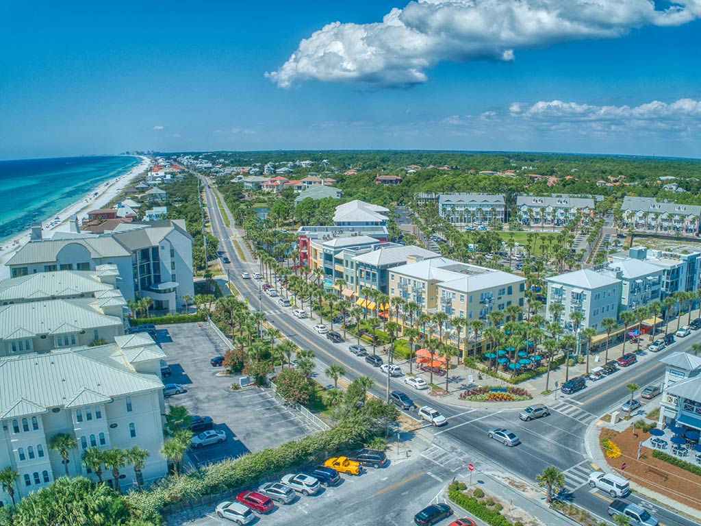 An aerial view of Gulf Place on the 30A in Santa Rosa Beach, FL, on a clear day, with the Gulf of Mexico on the upper left of the image, high-rise buildings in the foreground, and greenery in the distance on a clear day 