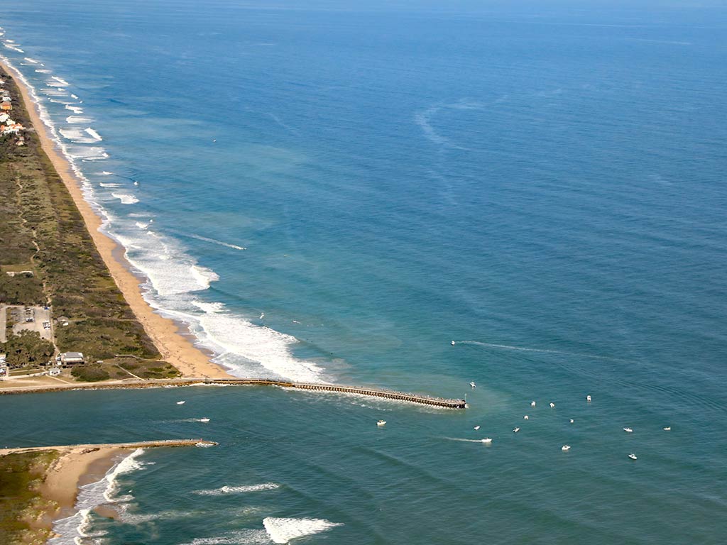 An aerial view of Sebastian Inlet on a clear day, with the inlet, beaches, and land visible on the left of the image, while the Atlantic Ocean dominates the rest of the photo