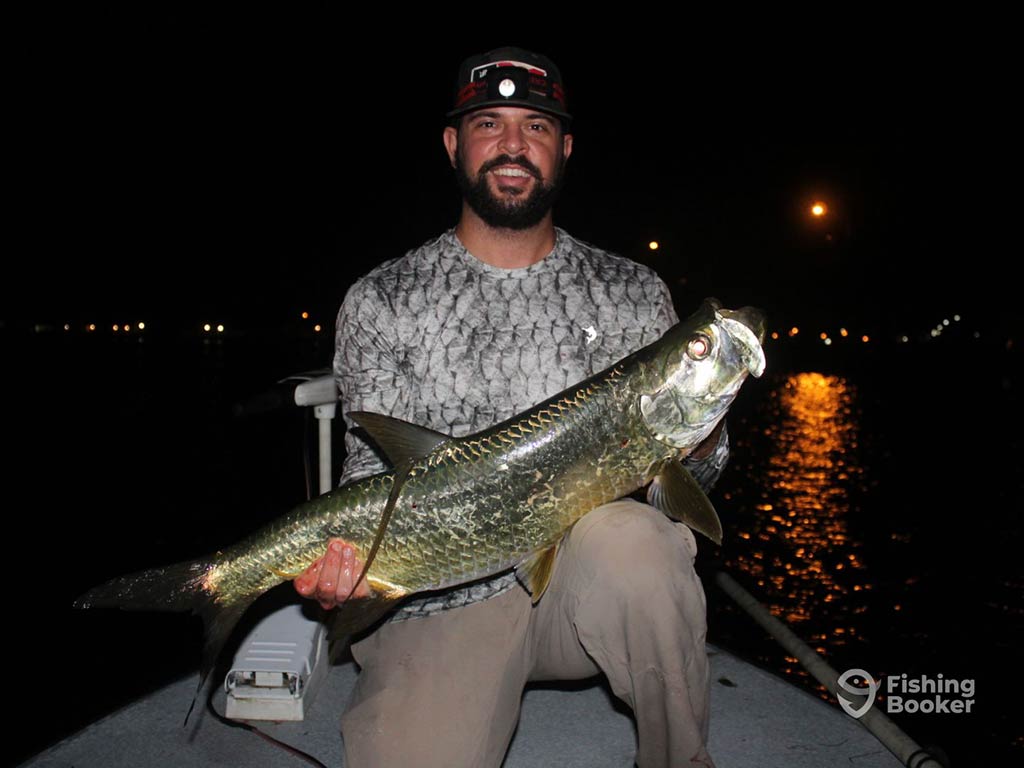 An angler wearing a headlamp, sitting on a fishing boat and holding a Tarpon at night