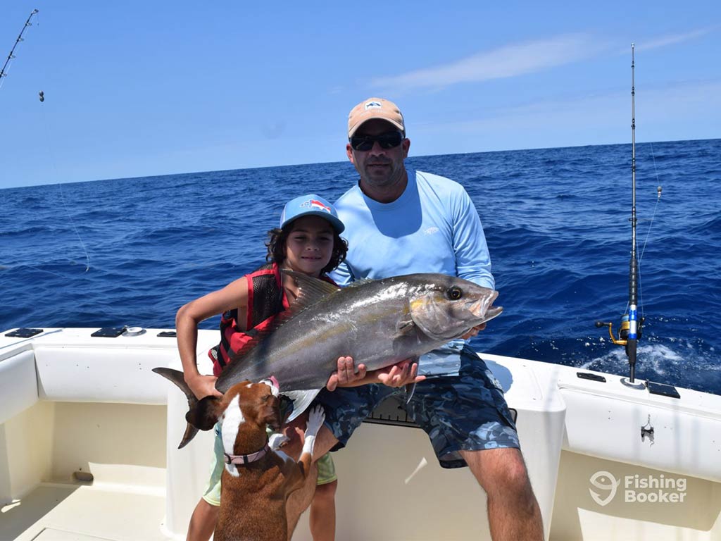 A father and son hold a Tilefish aboard a Wanchese fishing charter with the water behind them on a sunny day