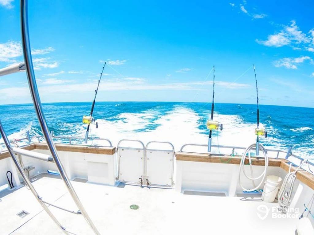 A view out from the back of fishing charter in Western Australia towards the open blue waters, with three trolling lines set up, trailing behind the boat, with the boat's wake visible, too, on a clear day