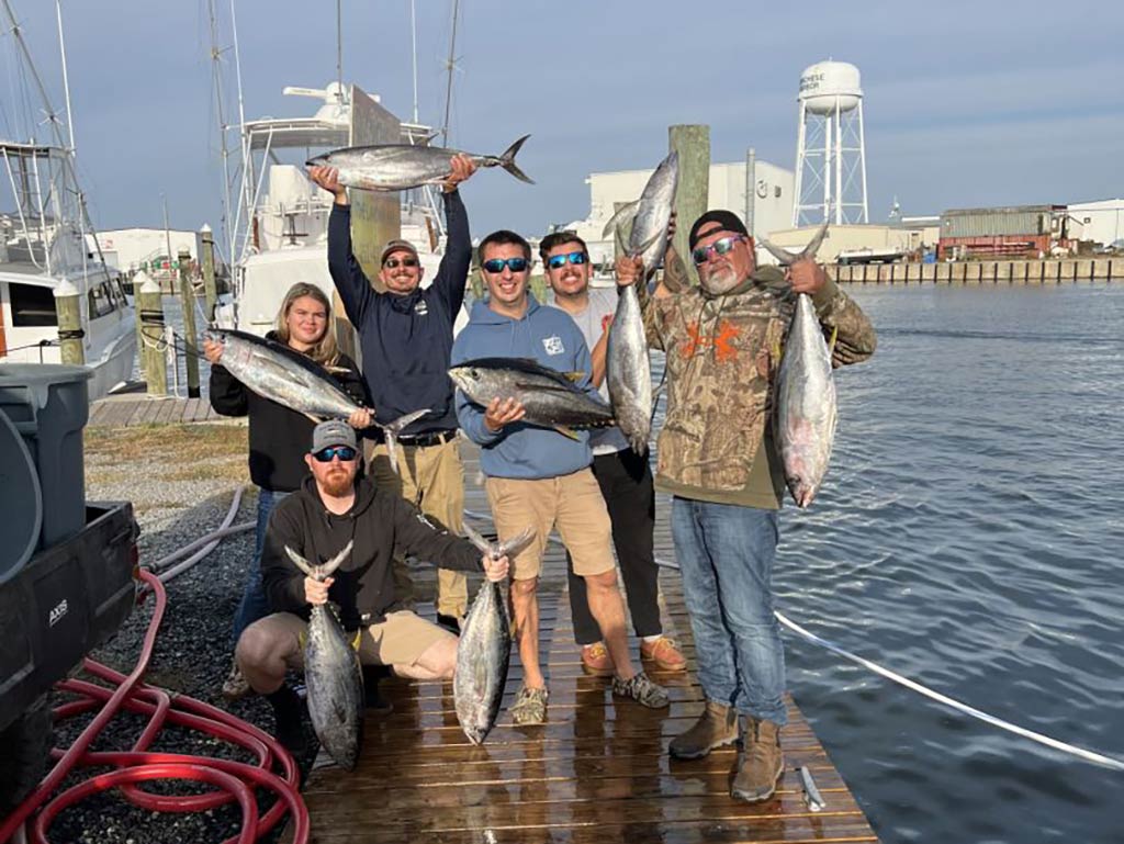 A group of anglers back on the dock in Manteo after a successful fishing trip, showing off their large haul of Tuna by holding them aloft on a sunny day