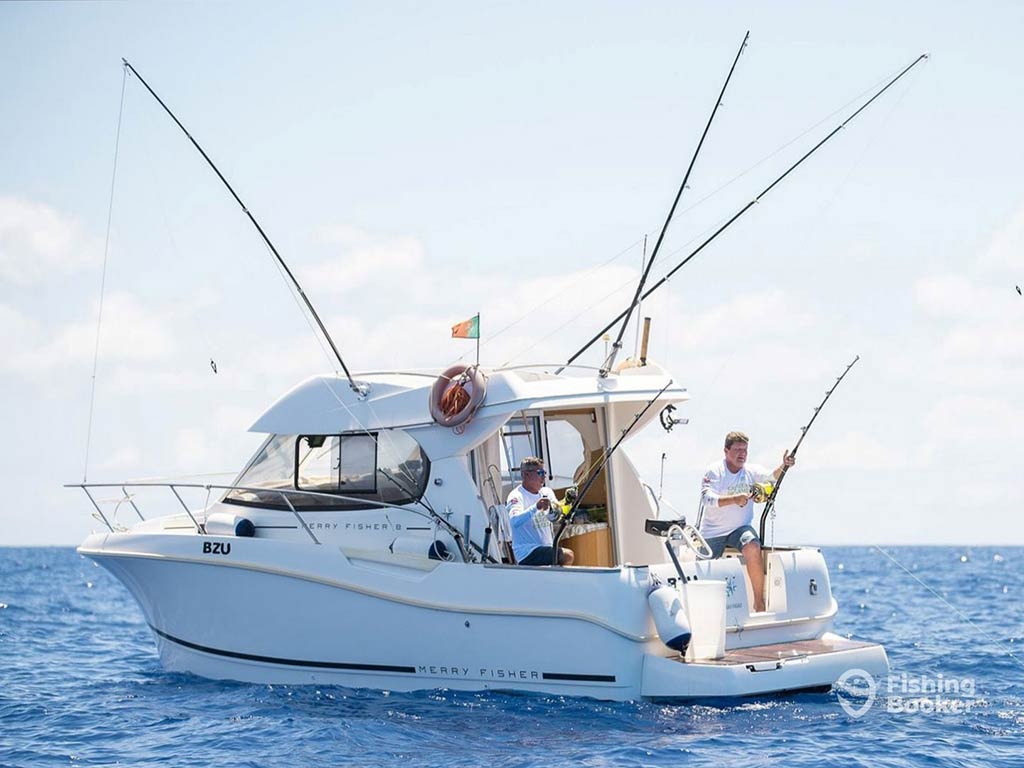 A view across the water towards a fishing charter, fully equipped with downriggers and outriggers, and two anglers standing on the deck fishing on a clear day