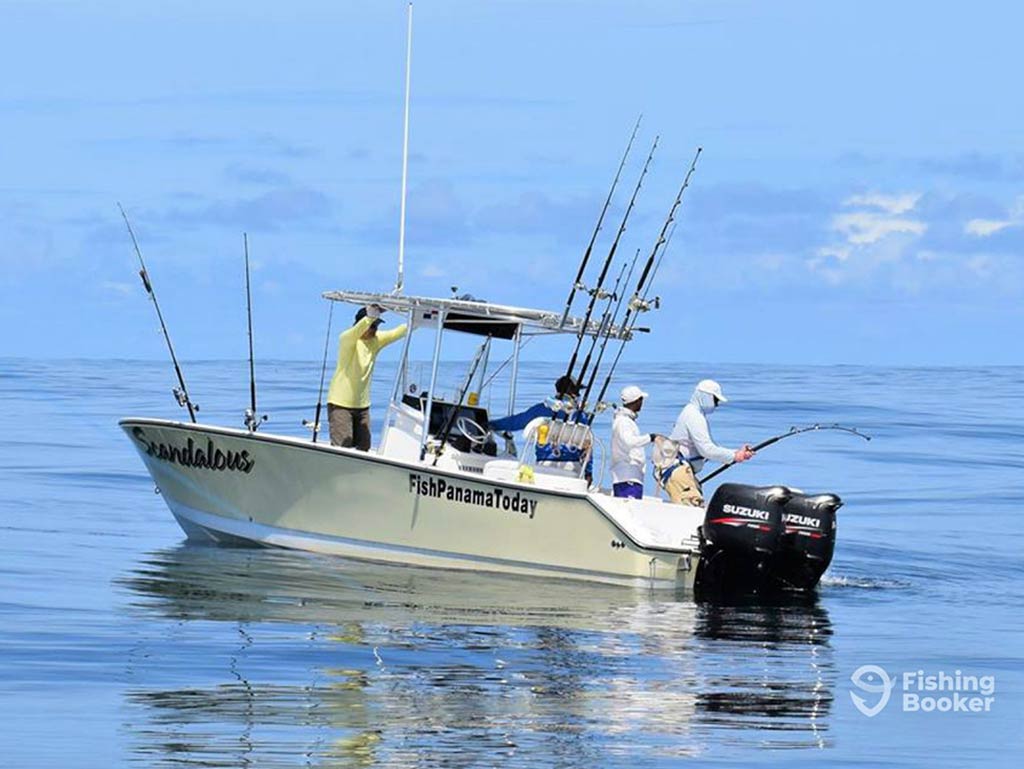 A view across calm waters towards a center console fishing boat in Panamá, geared up for trolling, but with two anglers on the deck fishing with rods on a day with sunny intervals