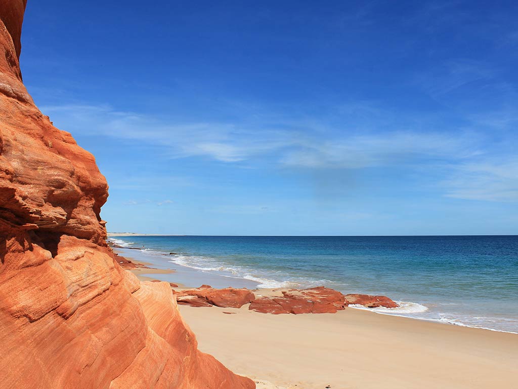 A view along the coastline in Kimberly Region, Western Australia, with red rocks on the left of the image and the Pacific Ocean in Coral Bay on the right on a clear day