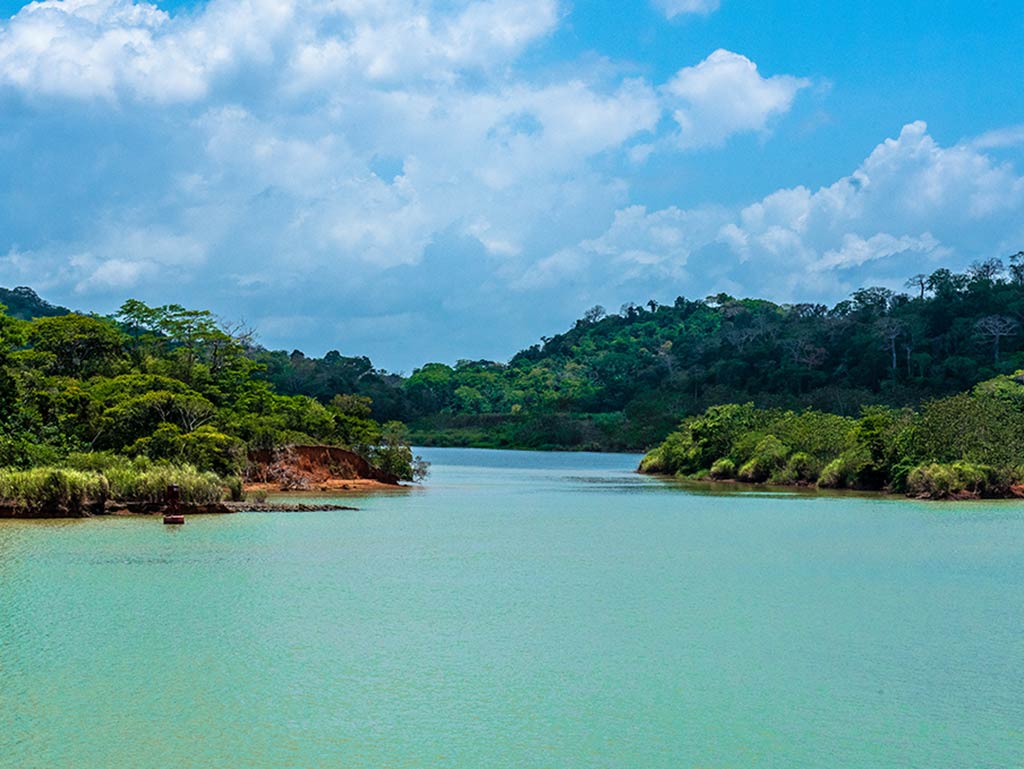 A view across the turquoise waters of Gatun Lake, Panamá to a point where it narrows, with tree-lined shores visible in the distance on a day with sunny intervals