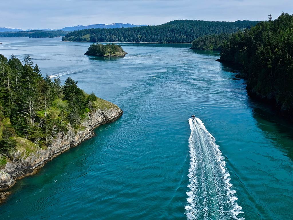 An aerial view of a boat making its way along a strait near Whidbey Island, with a smaller island visible in the distance on a cloudy day