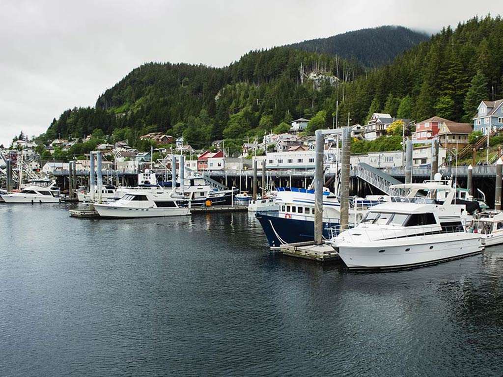 A view towards a harbor in Ketchikan, AK, on a cloudy day, with boats visible in the foreground and a green hill behind them