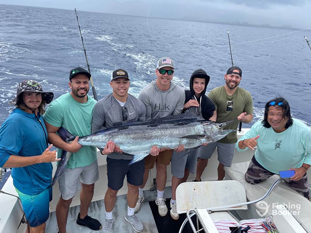 A group of anglers pose on the deck of an offshore sportfishing boat with a Marlin on a cloudy day in Hawaii