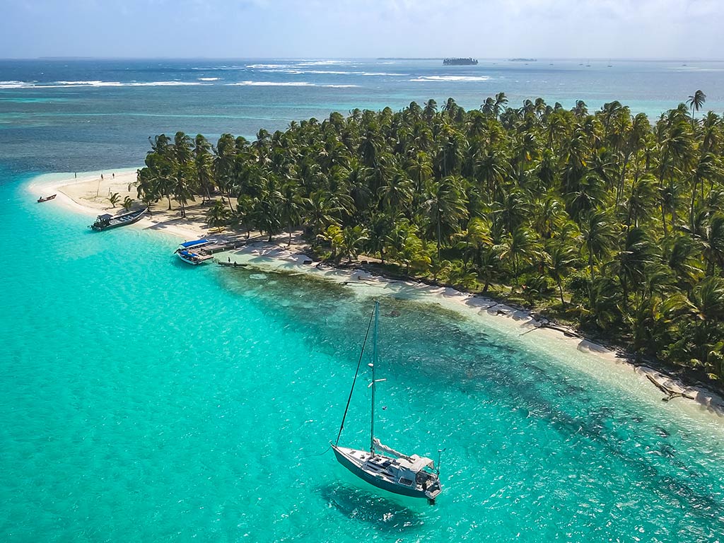 An aerial view of a sandy, green peninsula in Panamá, surrounded by turquoise water and one lone boat in the foreground on a sunny day