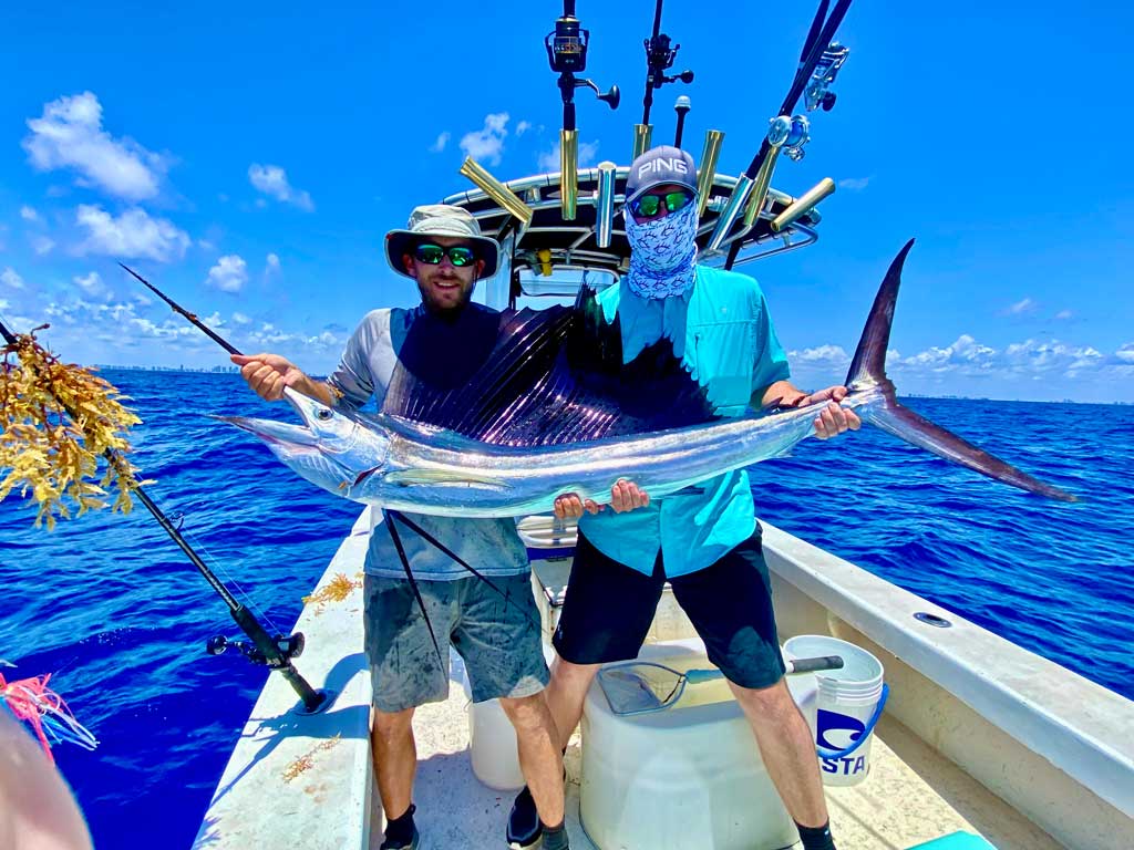 A photo of two proud anglers standing on a Miami fishing charter and holding a big Sailfish they caught on Labor Day weekend