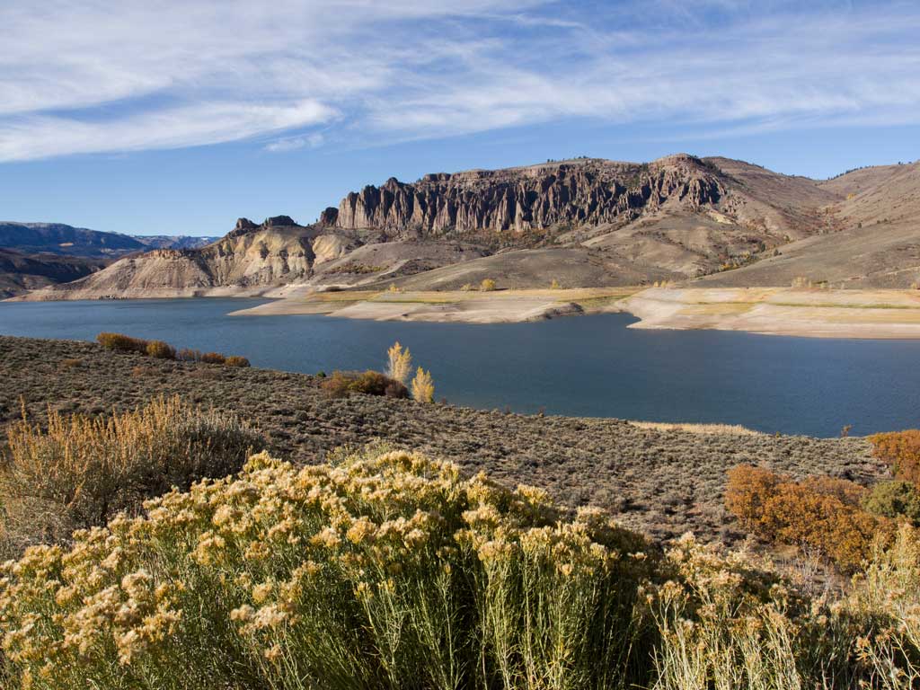 A view of the Blue Mesa Reservoir in Colorado near Gunnison as seen in the distance between a meadow in the front and the Dillon Pinnacles in the back