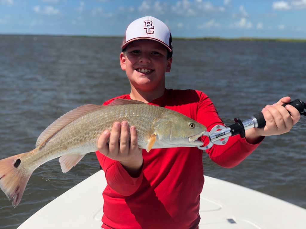 A photo of a boy standing on a Texas charter fishing boat while smiling and posing with a Redfish caught in Sabine Lake near Port Arthur in late summer