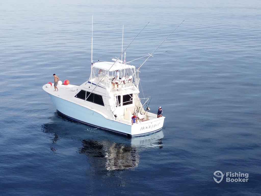 An aerial view of an offshore fishing charter in the calm, deep sea waters of Panamá, complete with outriggers for trolling and people on the deck and front of the boat