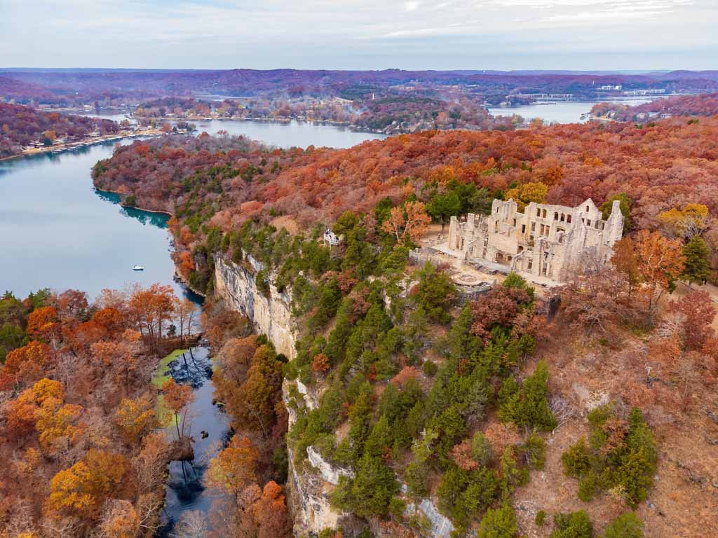 An aerial photo of Lake of the Ozarks, one of the best fall fishing destinations, and the surrounding forests and hills, with a dilapidated hilltop mansion visible.