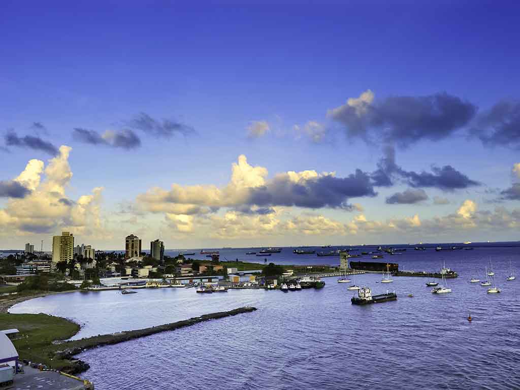 A view across a harbor in Panamá City, with boats visible in the foreground and the cityscape visible in the distance on a day with sunny intervals