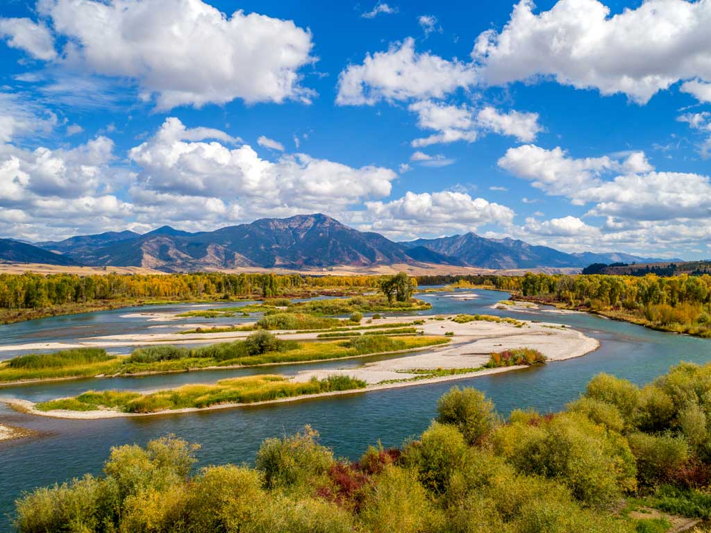 A stunning aerial view of the meandering Snake River in front of gorgeous mountains in the distance in Swan Valley, Idaho as seen on a bright and sunny day with cloud-dotted skies