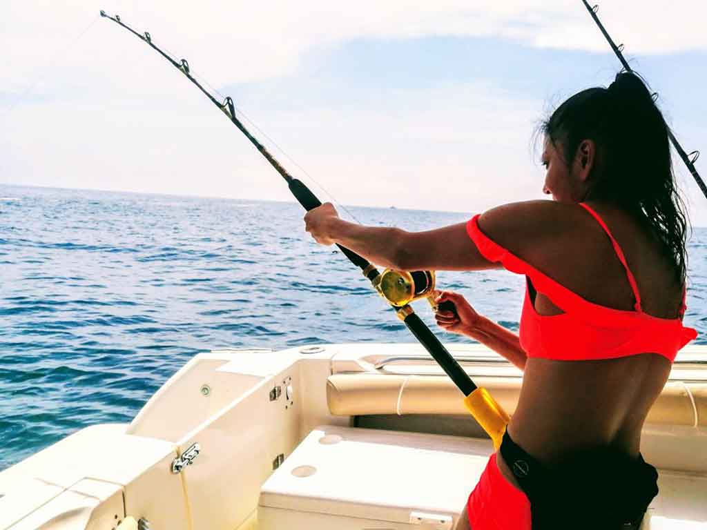 A woman in a bright pink bikini holding a heavy-duty fishing rod aboard an offshore fishing charter in Panamá on a sunny day