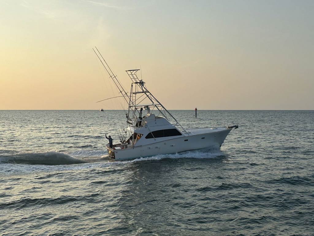 An offshore sportfishing boat, complete with a flybridge and outriggers gently makes its way back towards Key West at sunset, with no other boat around it on the open waters of the Florida Keys