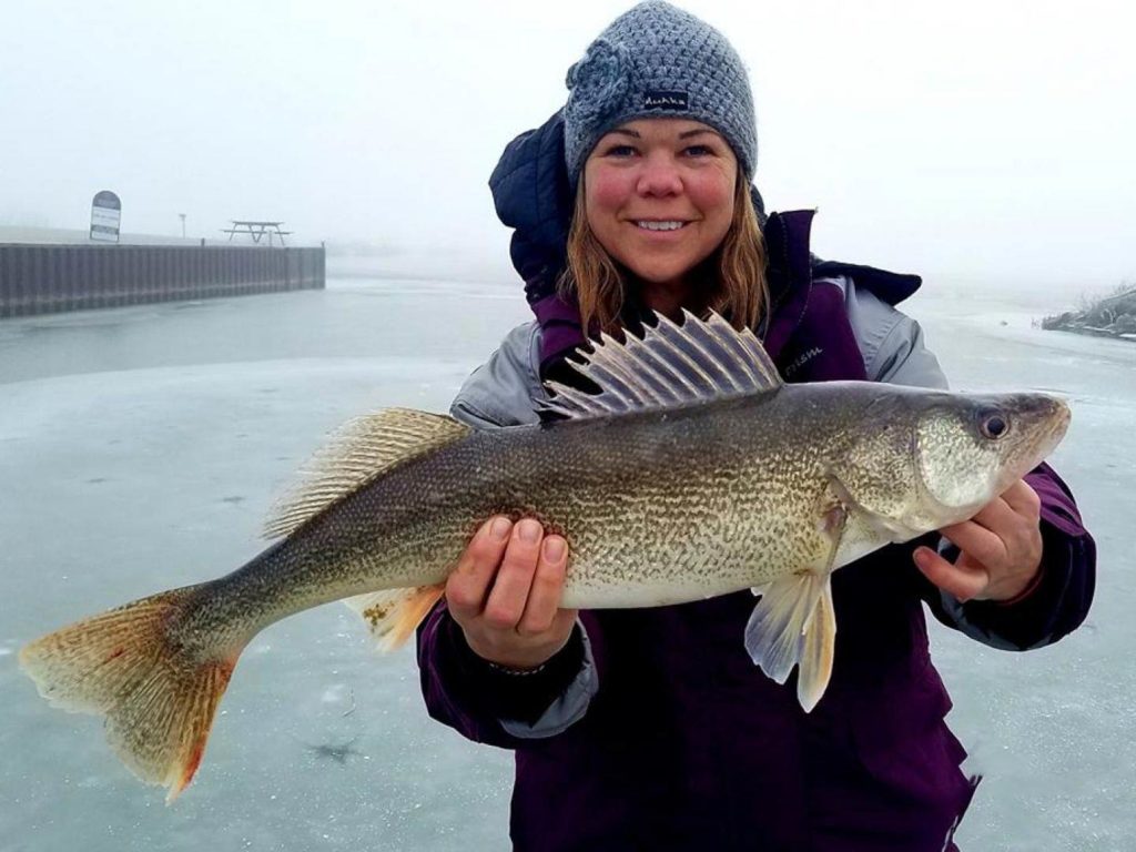 A woman holding a big Walleye while ice fishing