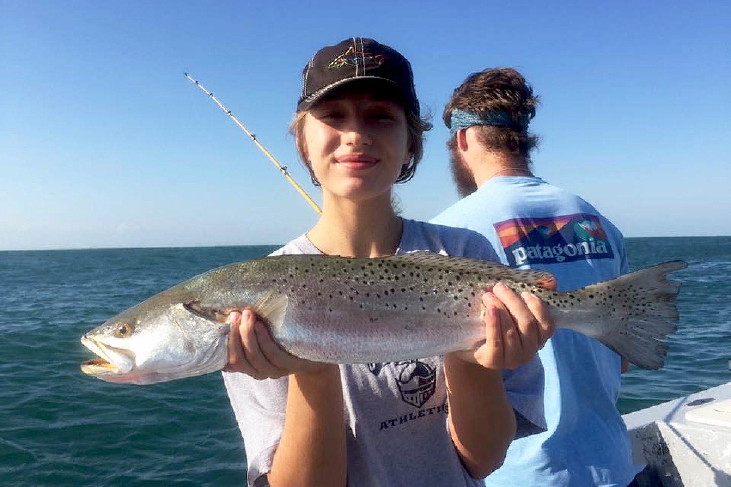 A girl holding a Speckled Trout on a boat in Texas smiling