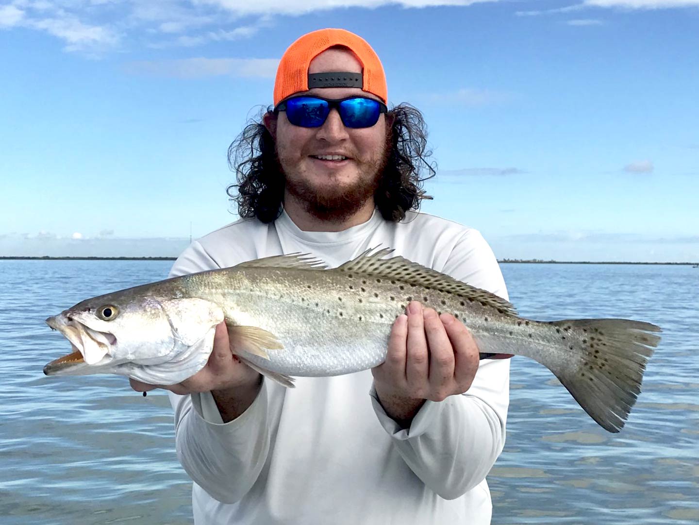 Ein Mann hält eine Speckled Trout auf einem Boot