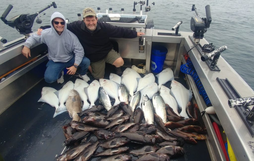 two smiling anglers posing on a boat full of fish in Alaska, showing that fishing is a great guilt-free activity to enjoy during the covid pandemic