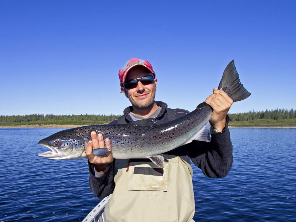 An angler holding a Salmon on a lake