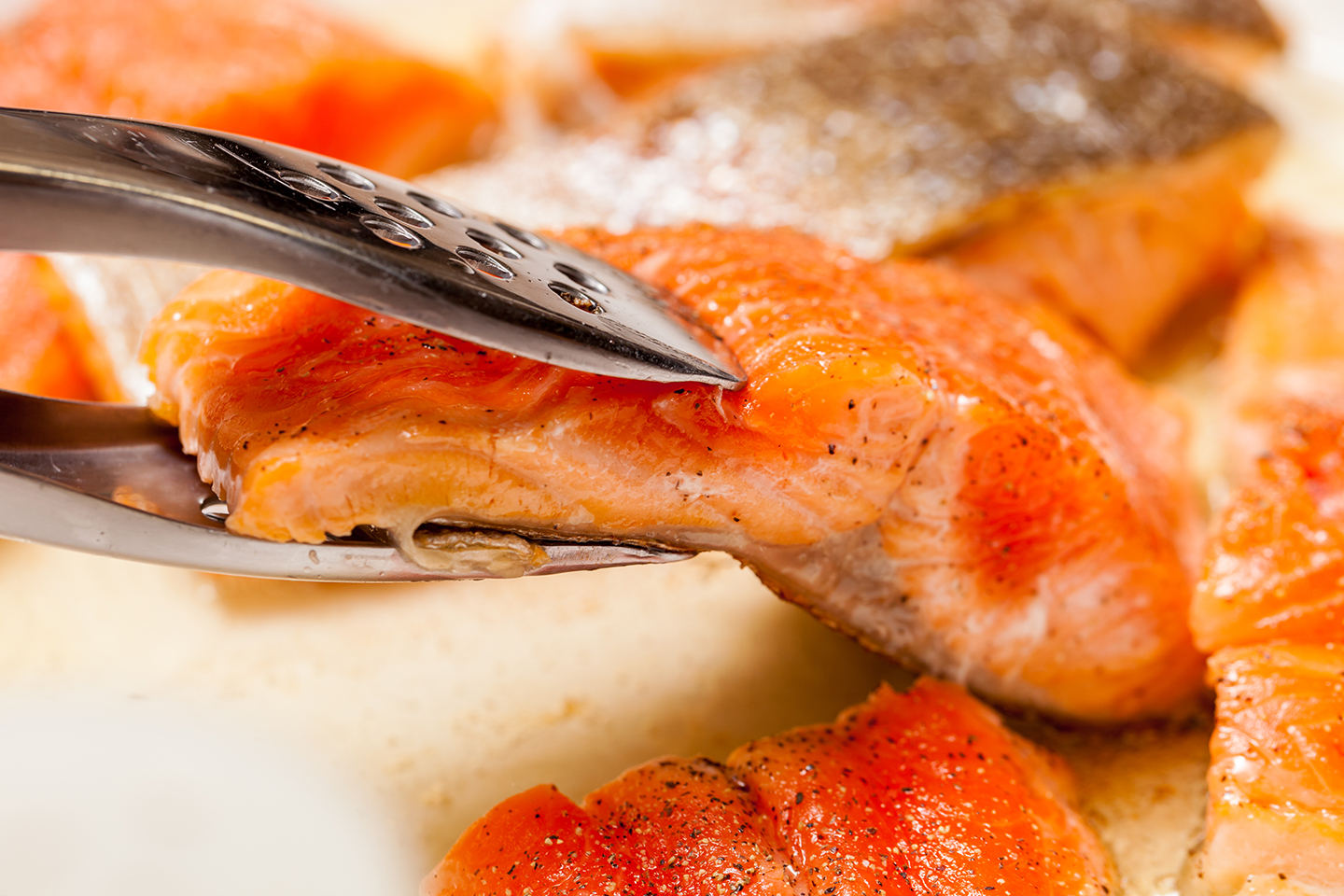 Piezas de salmón a la parrilla dadas la vuelta con unas pinzas metálicas