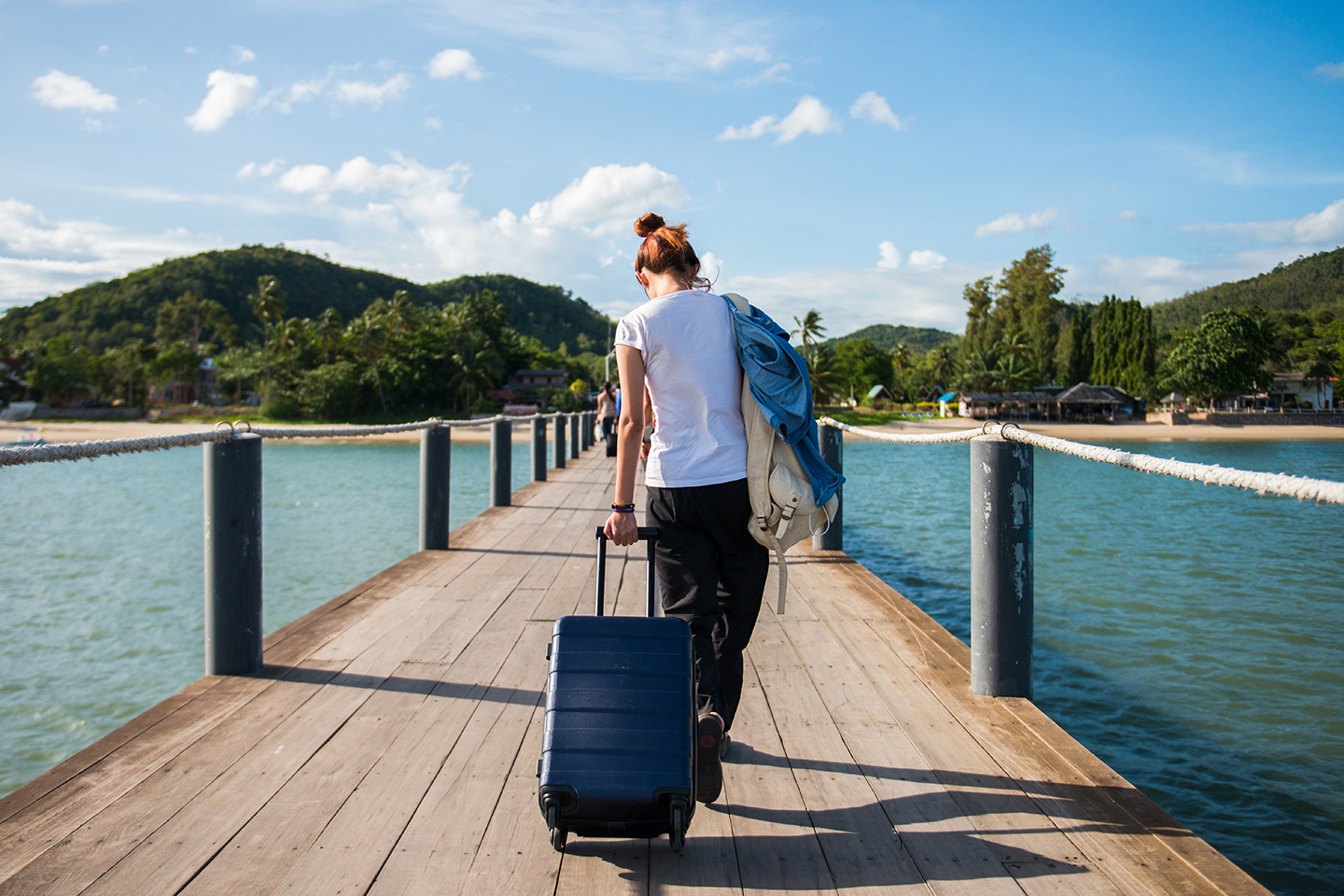 A woman walking along a wooden dock with a black suitcase
