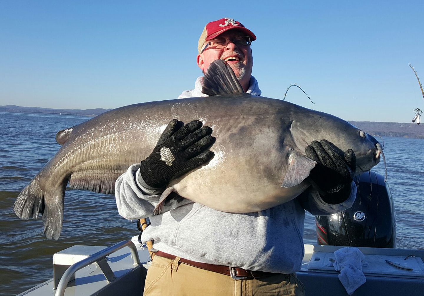 A happy man holding a big Blue Catfish on a boat with water and sky in the background