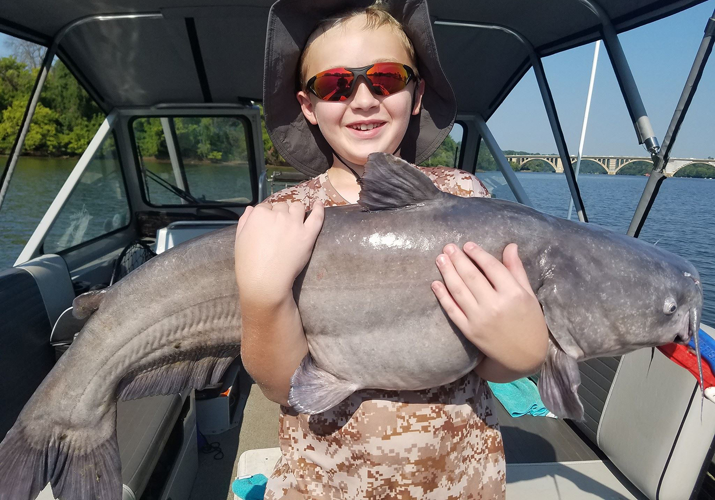 A happy child ion a boat holding a big Blue Cat caught on a catfishing trip.