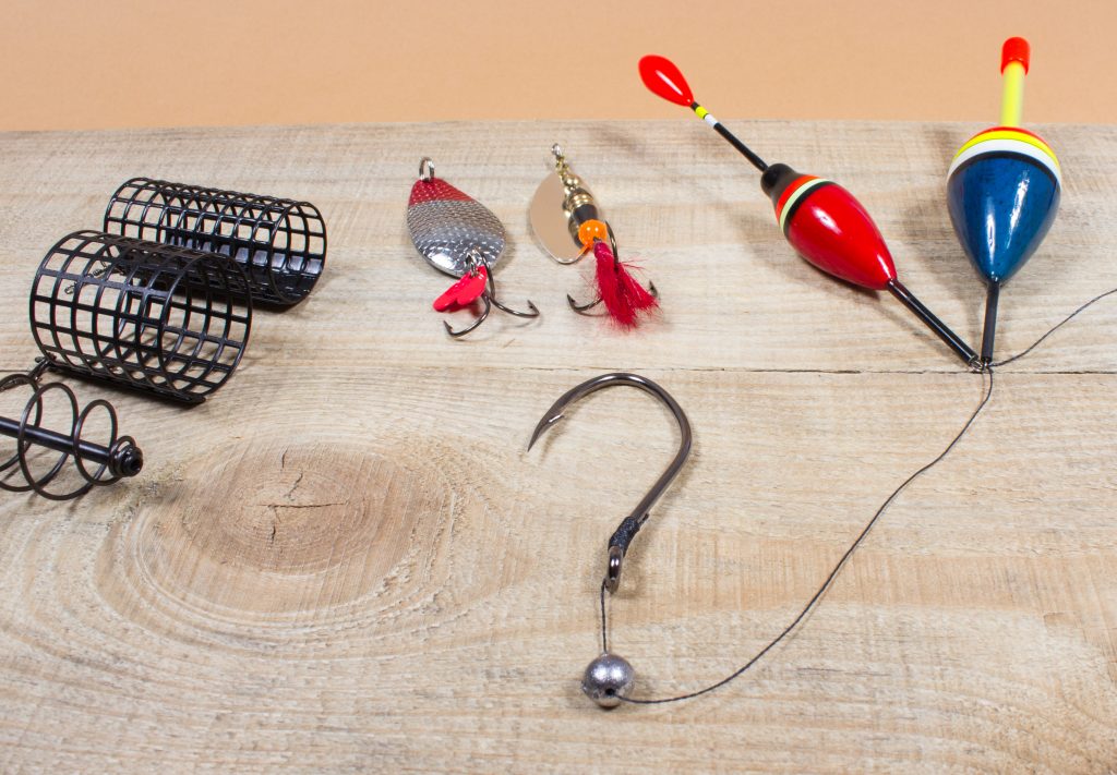 Assorted fishing tackle on a wooden table, with a hook and sinker making a question mark in the middle