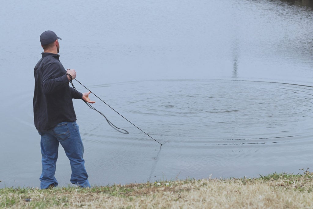 An angler standing by a lake pulling in a bait net on a catfishing trip