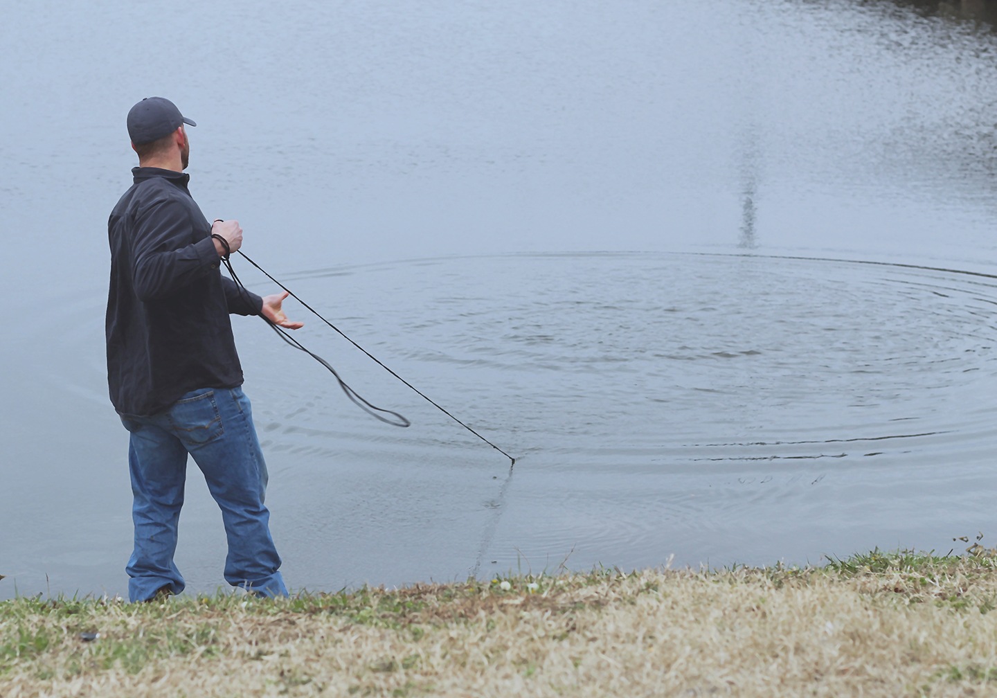 An angler standing by a lake pulling in a bait net on a catfishing trip