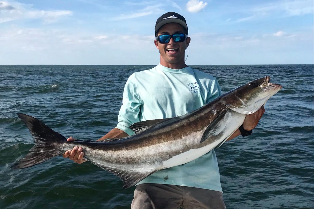 Een lachende visser houdt een grote Cobia vast op een boot.