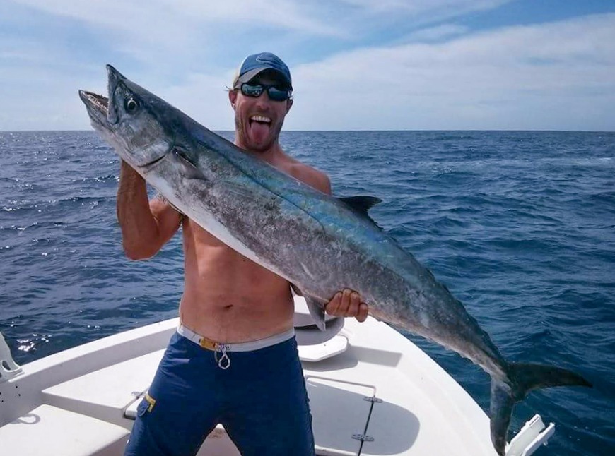 A smiling angler holding a big King Mackerel standing on a boat