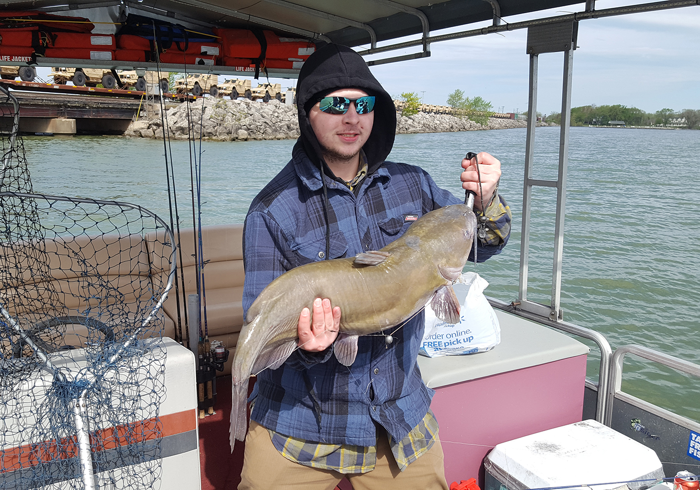 A male angler on a boat holding a Channel Catfish with a net on the left