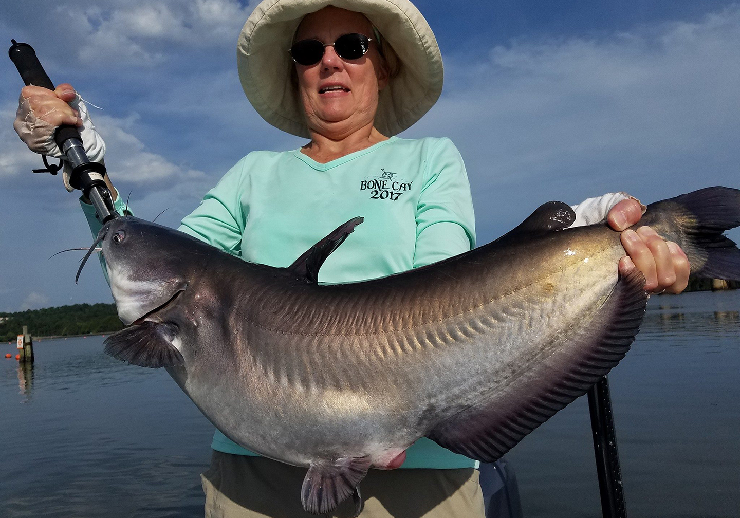 A lady holding a Catfish with water in the background