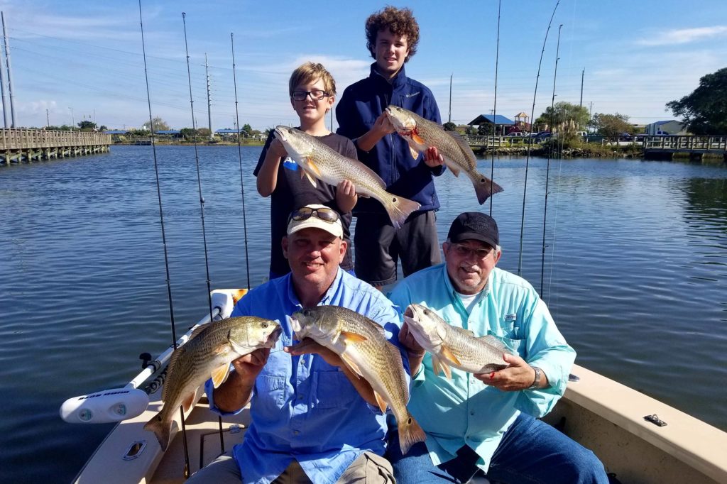 Two grownup anglers and two children sitting on a charter boat with their Redfish catches