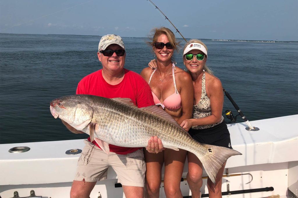 A man and two women hold a large Redfish caught inshore fishing in the Chesapeake Bay
